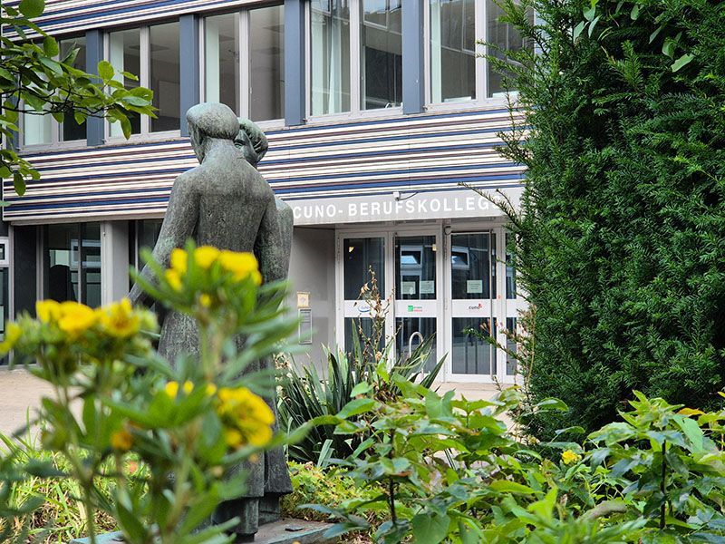 Foto Cuno Berufskolleg mit Statur und Blumen im Vordergrund